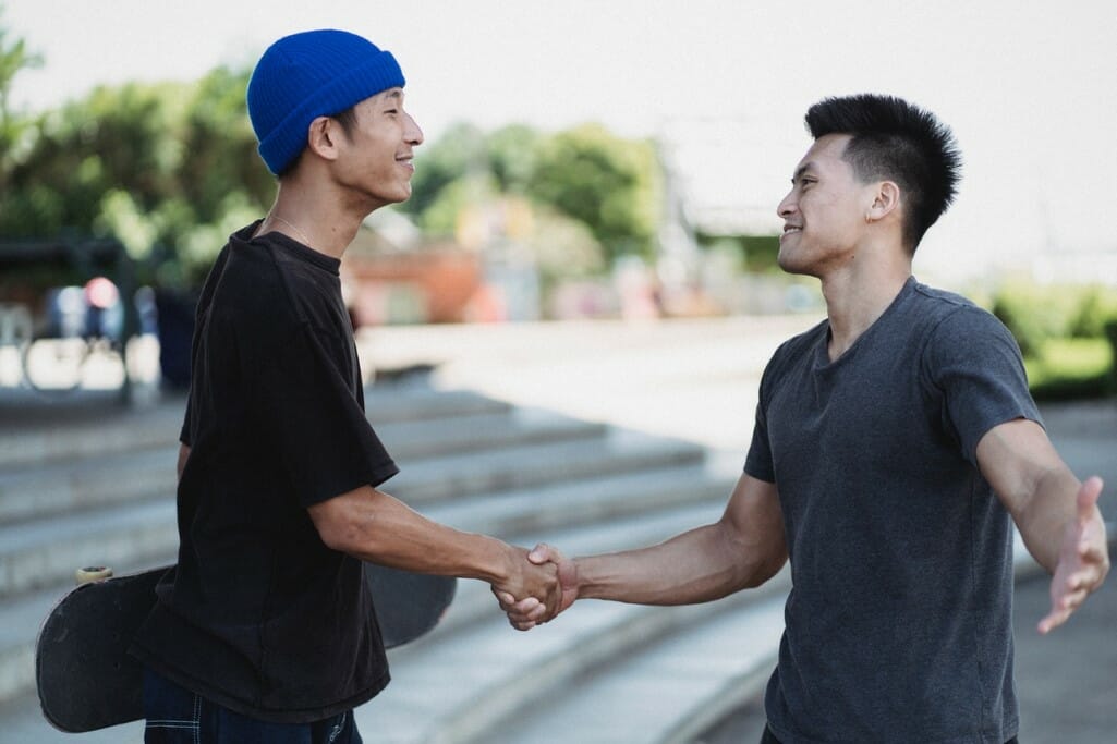 Two men shake hands and smile outside