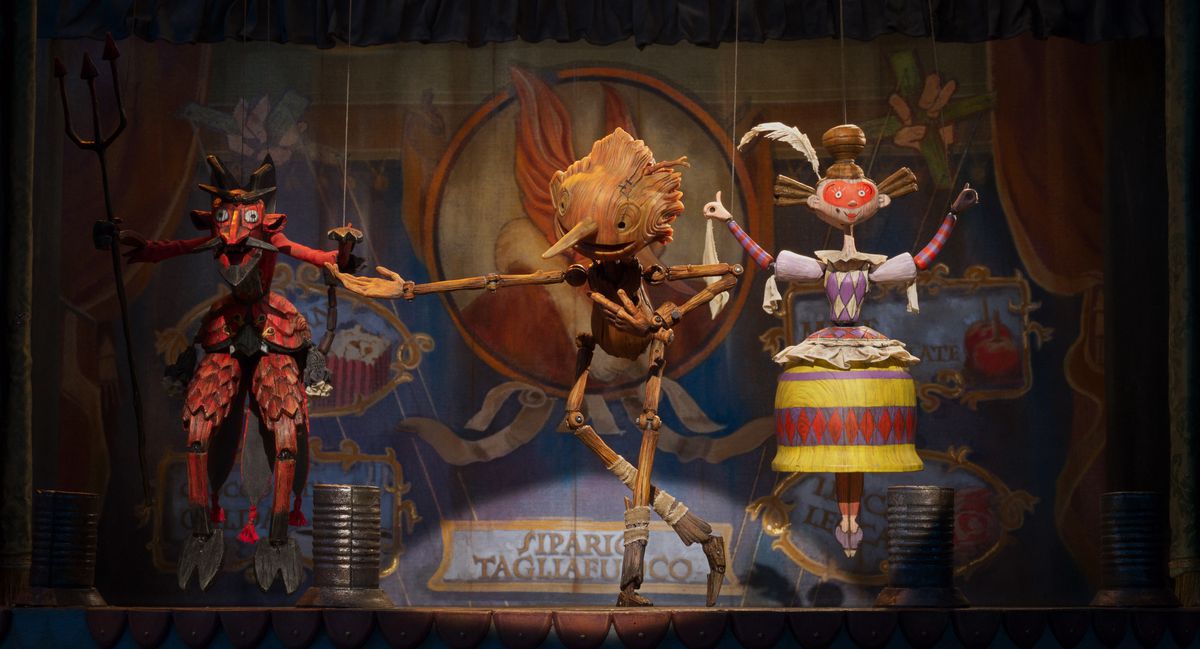 Pinocchio performs on stage next to puppets with strings in Guillermo del Toro’s Pinocchio.