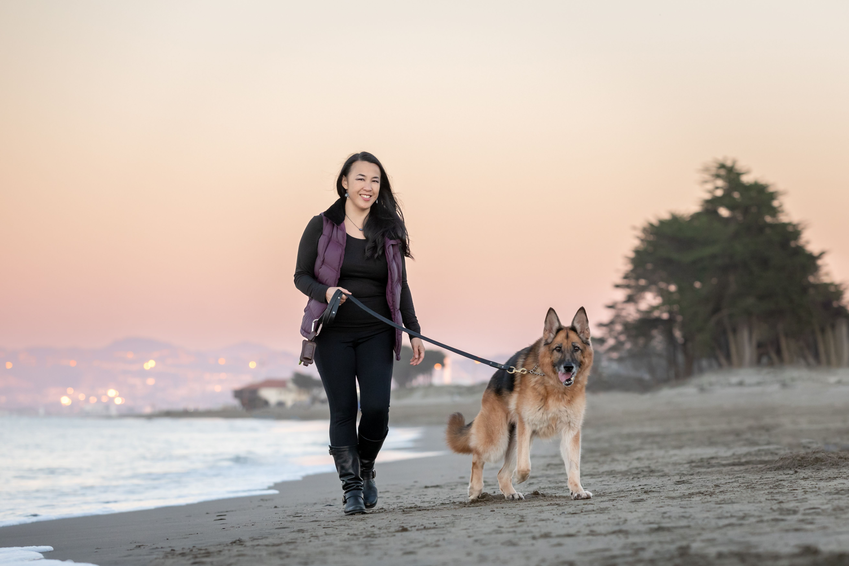 En kvinne og hunden hennes går langs stranden ved solnedgang