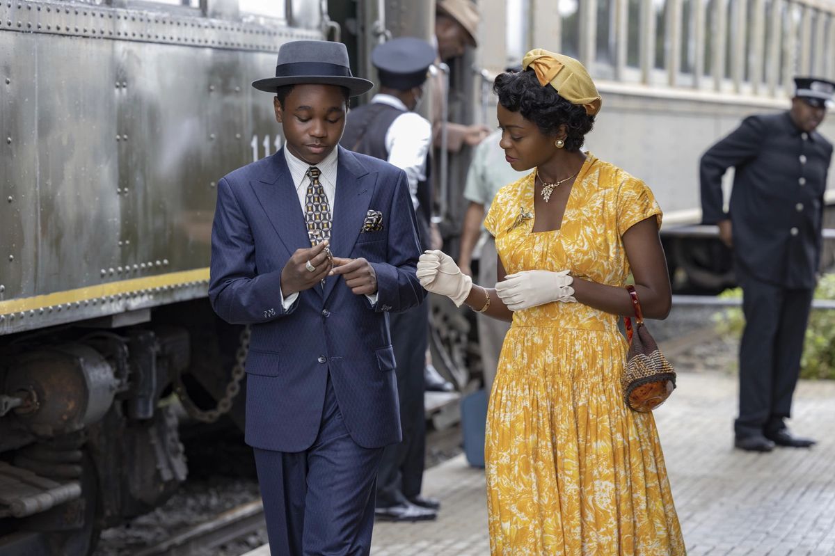 Un ragazzo in abito blu scuro (Jalyn Hall) è in piedi accanto a una donna in abito giallo (Danielle Deadwyler) accanto a una locomotiva.