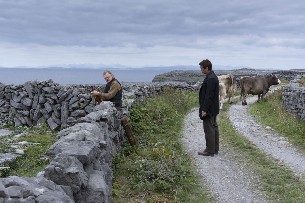 Pádraic (Colin Farrell) tries to speak to his former friend Colm (Brendan Gleeson) while both men are standing in a rutted lane by a donkey cart, surrounded by low stone fences, in The Banshees of Inisherin