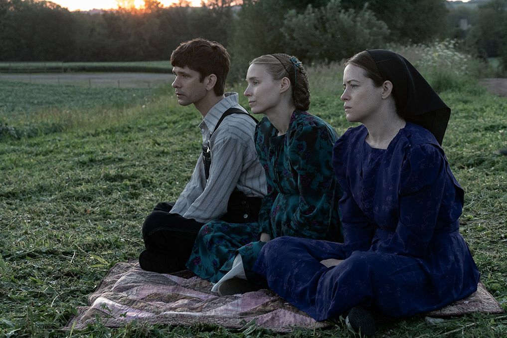 Ben Whishaw, Rooney Mara, and Jessie Buckley sit on a blanket in the grass in Women Talking.