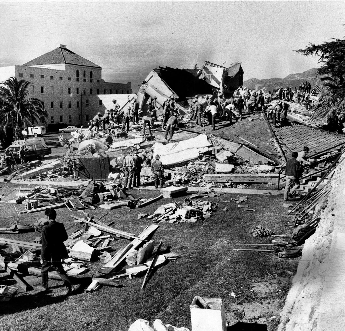 People stand near a large collapsed building.