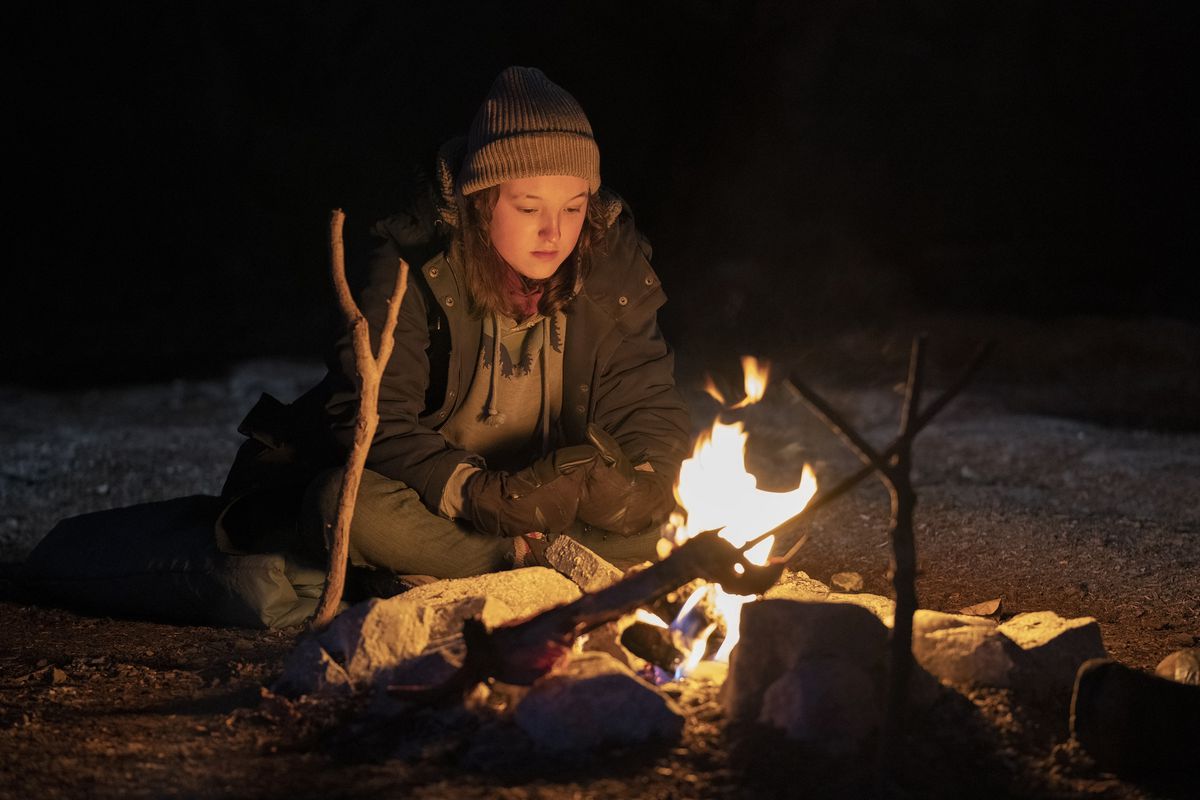 Bella Ramsey sits alone by a campfire in The Last of Us.
