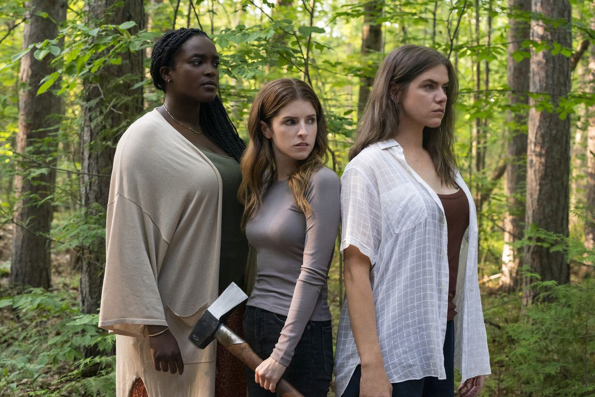 Three women (L-R: Sophie (Wunmi Mosaku), Alice (Anna Kendrick), Tess (Kaniehtiio Horn)) stand in a forest, one of them holding an axe in their left hand.
