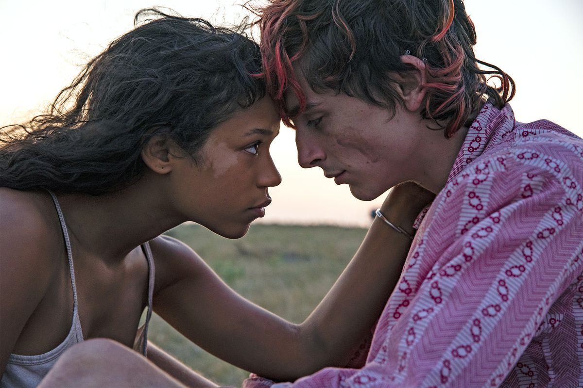 Uma jovem (Taylor Russell) coloca a testa contra um jovem (Timothee Chalamet) com mechas de tinta rosa no cabelo.