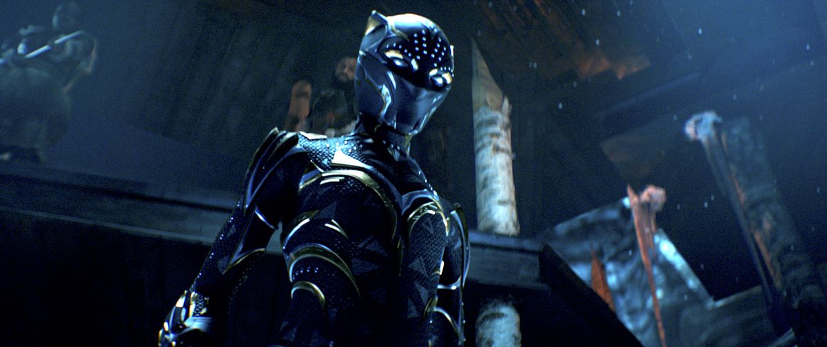 Shuri w swoim przetykanym złotem kostiumie Czarnej Pantery, stojąca w ciemnej sali tronowej, w Black Panther: Wakanda Forever