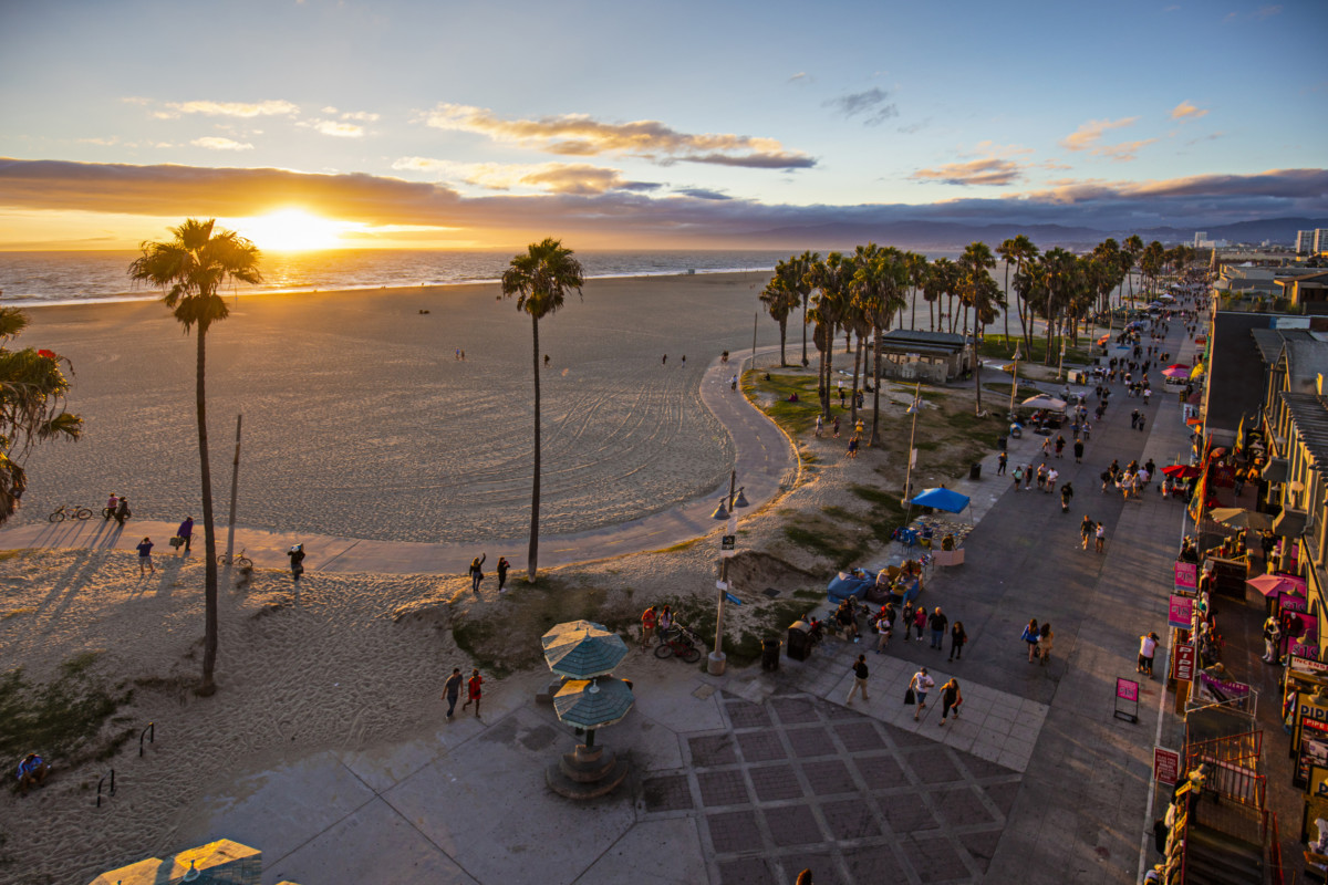 Туристи, що йдуть по доріжці біля пляжу під час заходу сонця _ Гетті