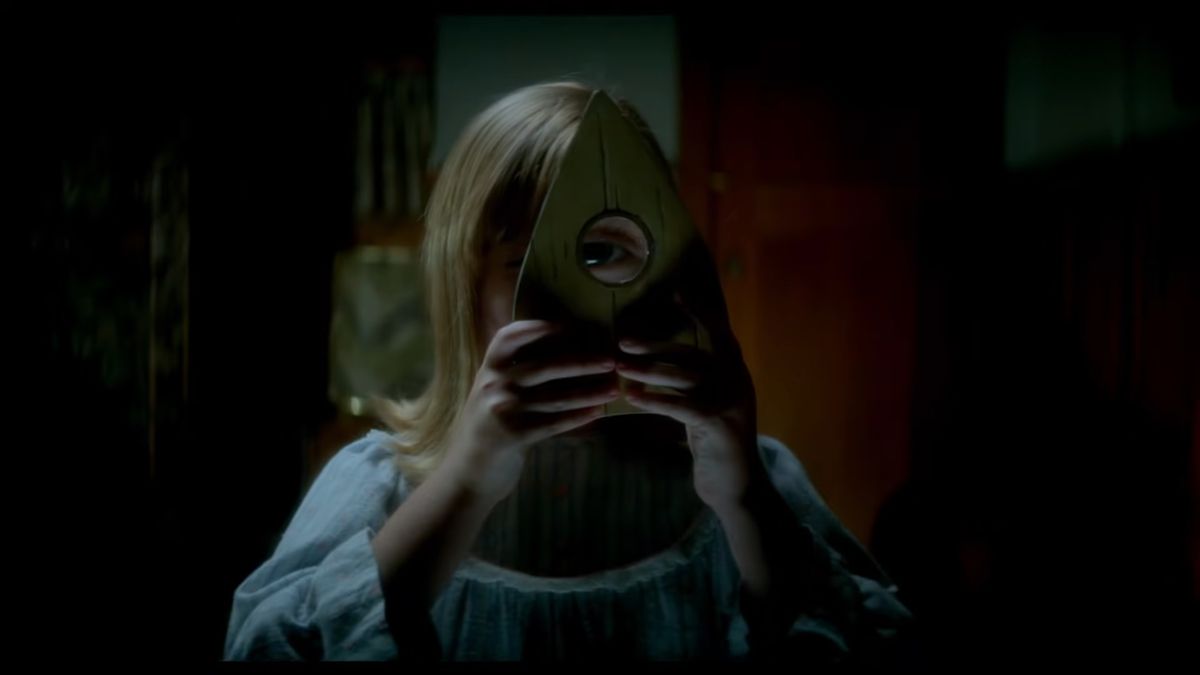 Молодая девушка смотрит через планшетку для спиритических сеансов в Ouija: Origin of Evil.