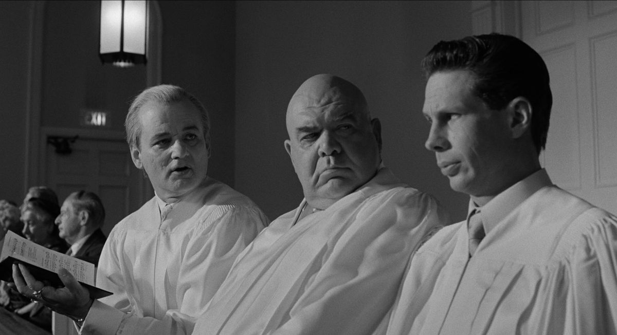 George “The Animal” Steele sits next to Bill Murray while wearing all white in Ed Wood. They both look at the man next to them.