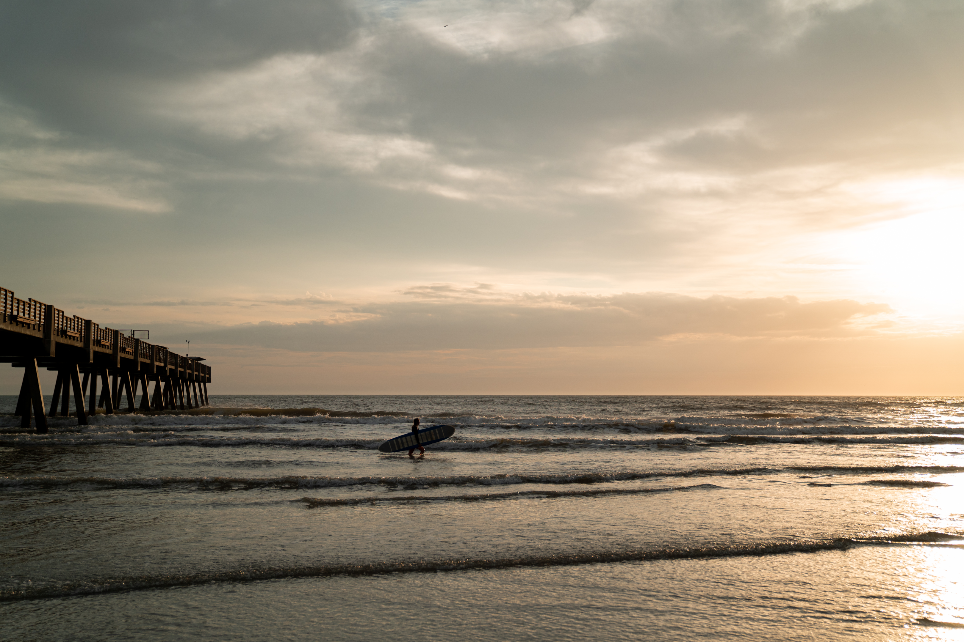 Pantai Atlantik dengan peselancar di luar saat matahari terbenam