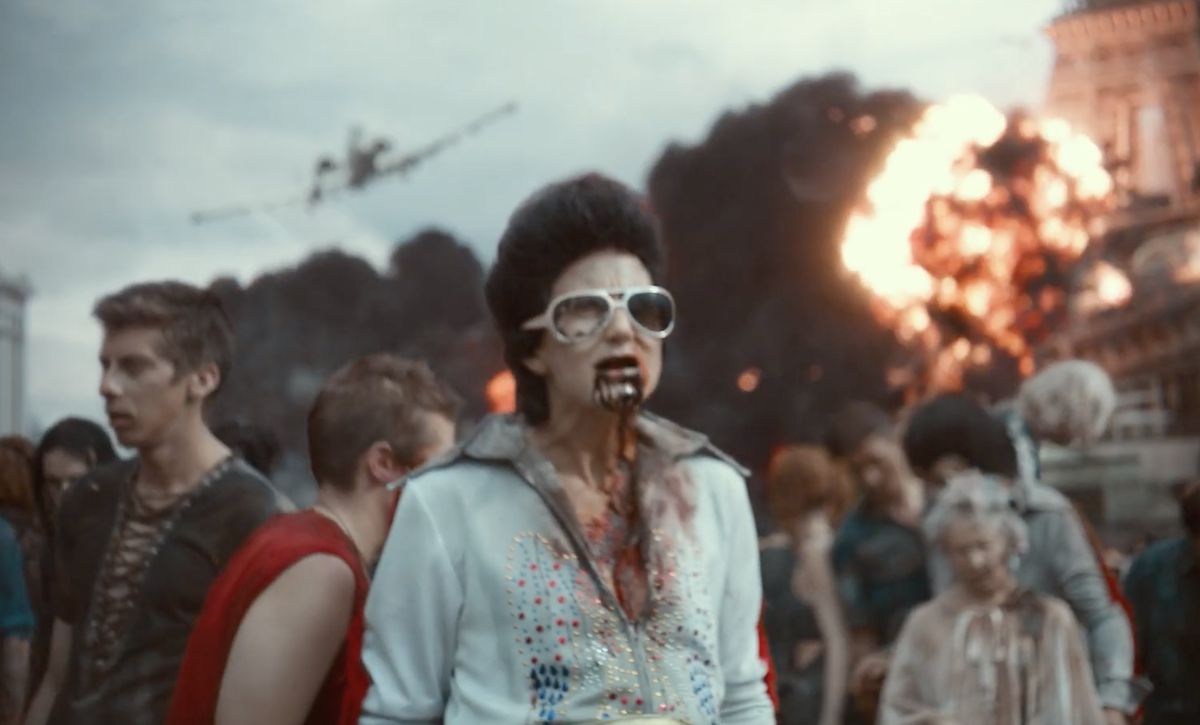 A zombie Elvis impersonator wonders around Vegas with other zombies as an explosion happens behind them in Army of the Dead.