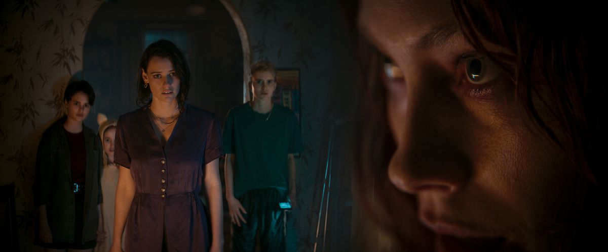 Beth (Lily Sullivan) nervously confronts her disturbed-looking syster Ellie (Alyssa Sutherland) as Ellie’s three kids huddle behind her in a dark doorway in Evil Dead Rise