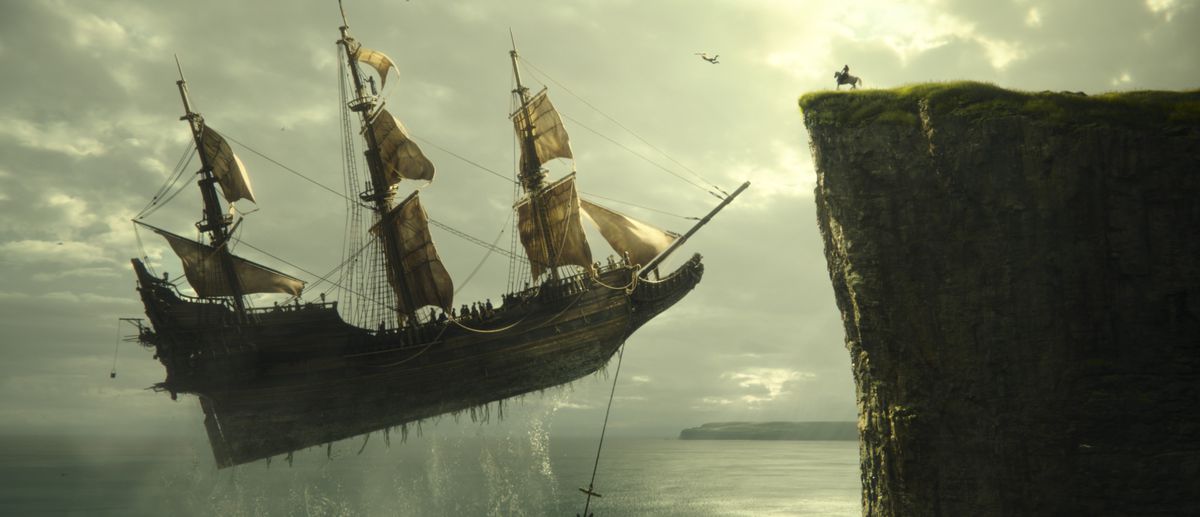 A flying ship with sails hovers over the water and approaches a cliffside, where a figure sits on a horse in Peter Pan and Wendy.