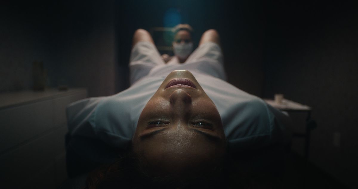 A close-up shot of a woman (Dianna Agron) in a hospital gown lying down on a table as a nurse examines between her legs in Clock.