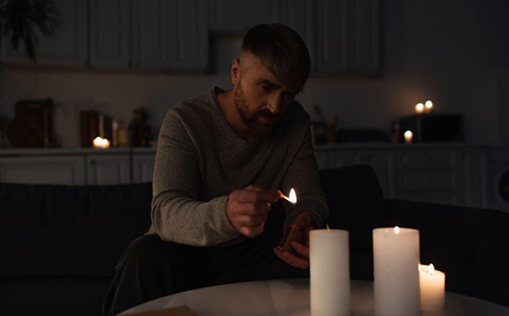 Outages Man Sits in Dark Lights Candle