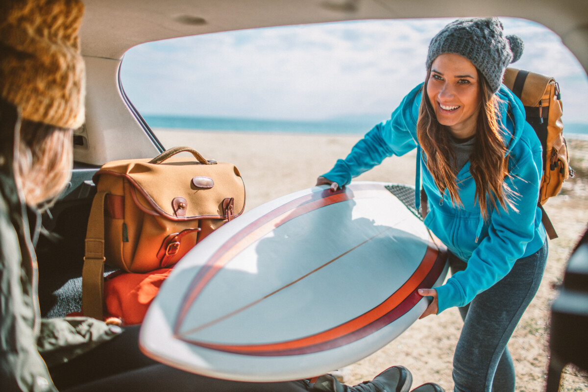 Fotografie cu o fetiță surfer care își face bagajele pentru o excursie de surfing: punând o placă de surf în portbagajul mașinii