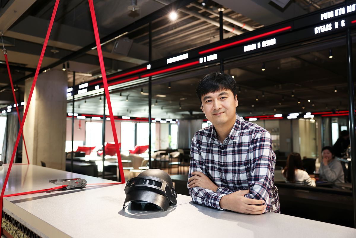 A photo of Sangkyun Kim of PUBG Studios standing, arms crossed, near a PUBG helmet