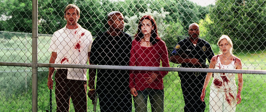 The bloodied cast of Zack Snyder’s Dawn of the Dead stands behind a chain-link fence