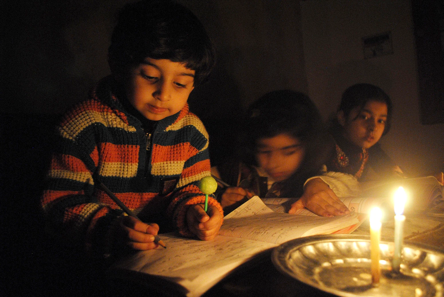 เด็กๆ เรียนหนังสือใต้แสงเทียนระหว่างไฟฟ้าดับในเมืองเปชาวาร์ทางตะวันตกเฉียงเหนือของปากีสถาน มกราคม 2015
