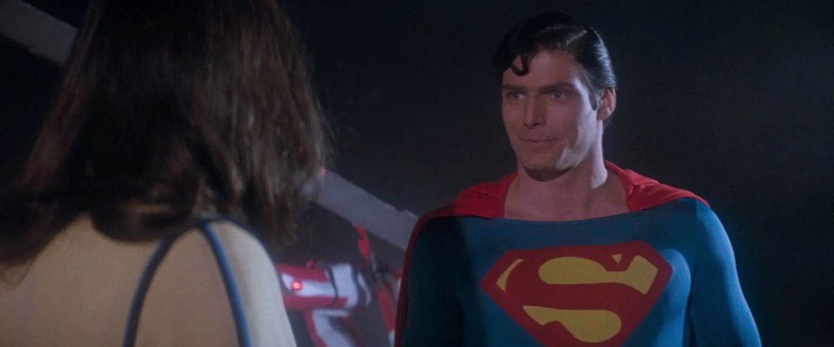 Christopher Reeve as Superman faces Margot Kidder as Lois Lane, with a small quirky smile on his face in Superman (1978).