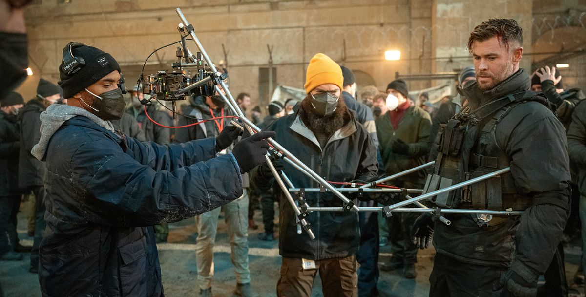 Director Sam Hargrave and a camera operator attach a camera to Chris Hemsworth’s chest with a series of telescoping, jointed silver poles for part of Extraction 2’s oner sequence