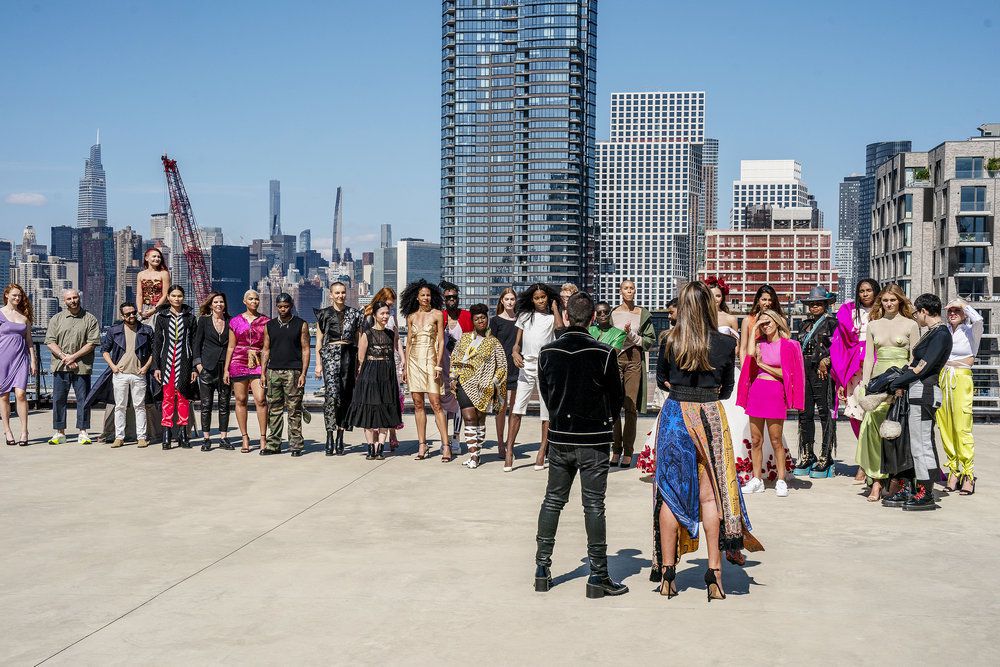 The cast of Project Runway season 20 standa nd listen to the hosts in front of a New York skyline