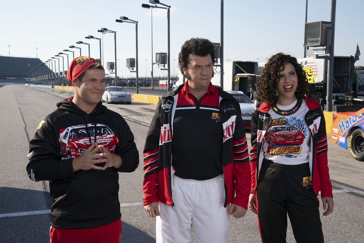 The Gemstone kids (Adam Devine, Danny McBride, and Edi Patterson) stand in racing attire on a racing track