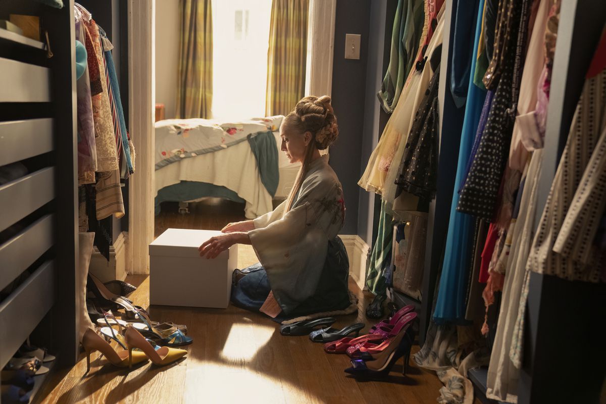 Carrie (Sarah Jessica Parker) sitting in her closet opening a box in a still from And Just Like That... season 2
