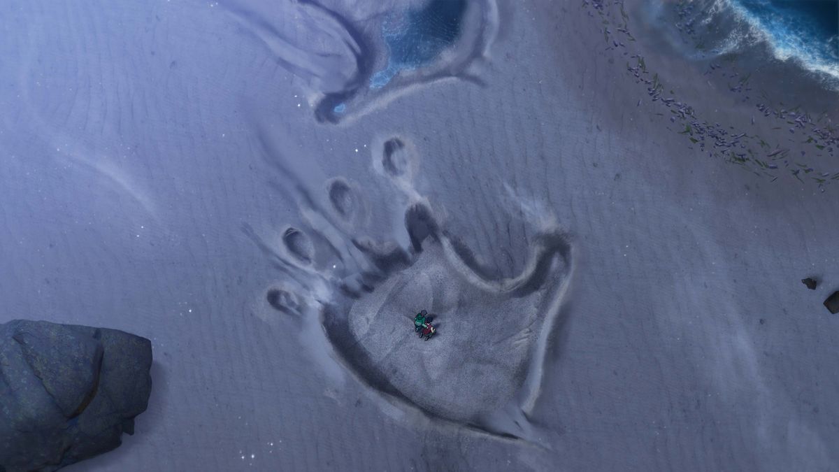 Two people stand in the sand imprint of a giant monkey paw