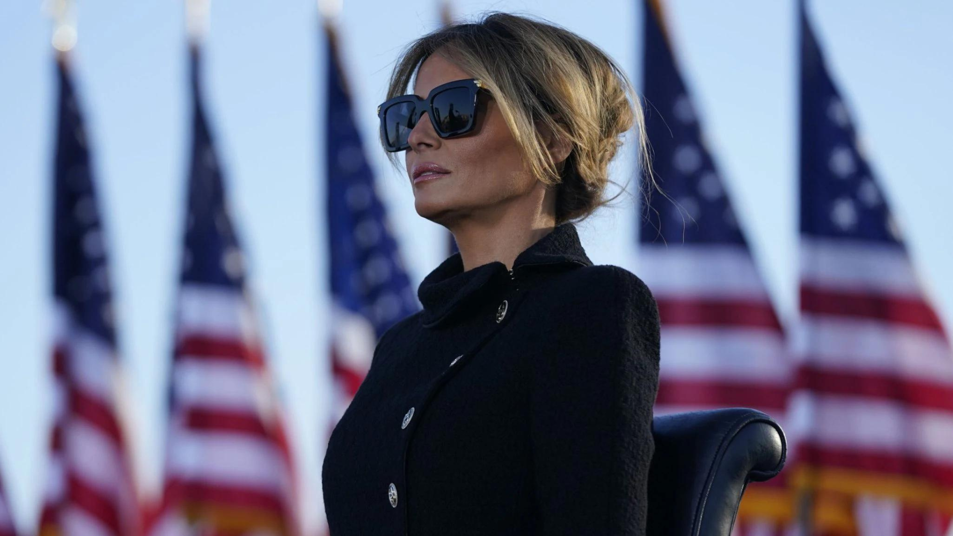 A Picture of Melania Trump, who recently launched a new NFT collection, standing in front of a row of american flags