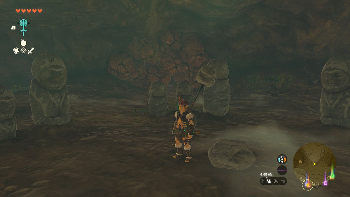 Link stands behind three stone statues facing the path forward inside the cave in Zelda: Tears of the Kingdom