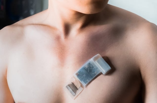 A photo showing the upper part of a person's bare chest, with the ultrasound chip stuck to the skin over their heart. The chip is smaller than a credit card and is not attached to any wires.