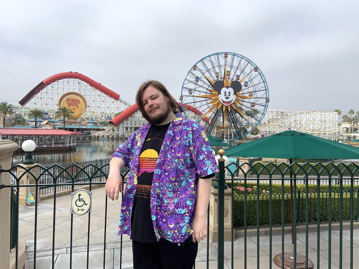 A man wearing a shirt covered in Pokemon characters stands in front of a ferris wheel at Disney’s California Adventure.
