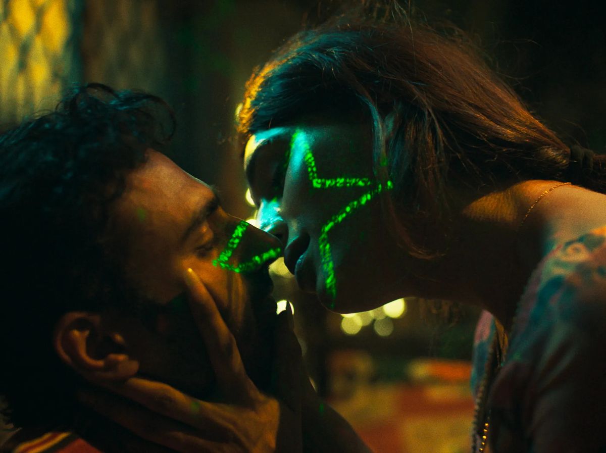 (L-R) Ali Junejo and Rasti Farooq leaning towards one another to kiss with a green light shaped like a star visible on the latter’s face in Joyland.