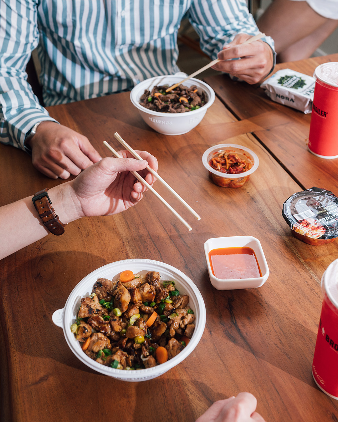 people sitting at the table eating bowls from the Flame Broiler with hashi and sauces - The Flame Broiler meu