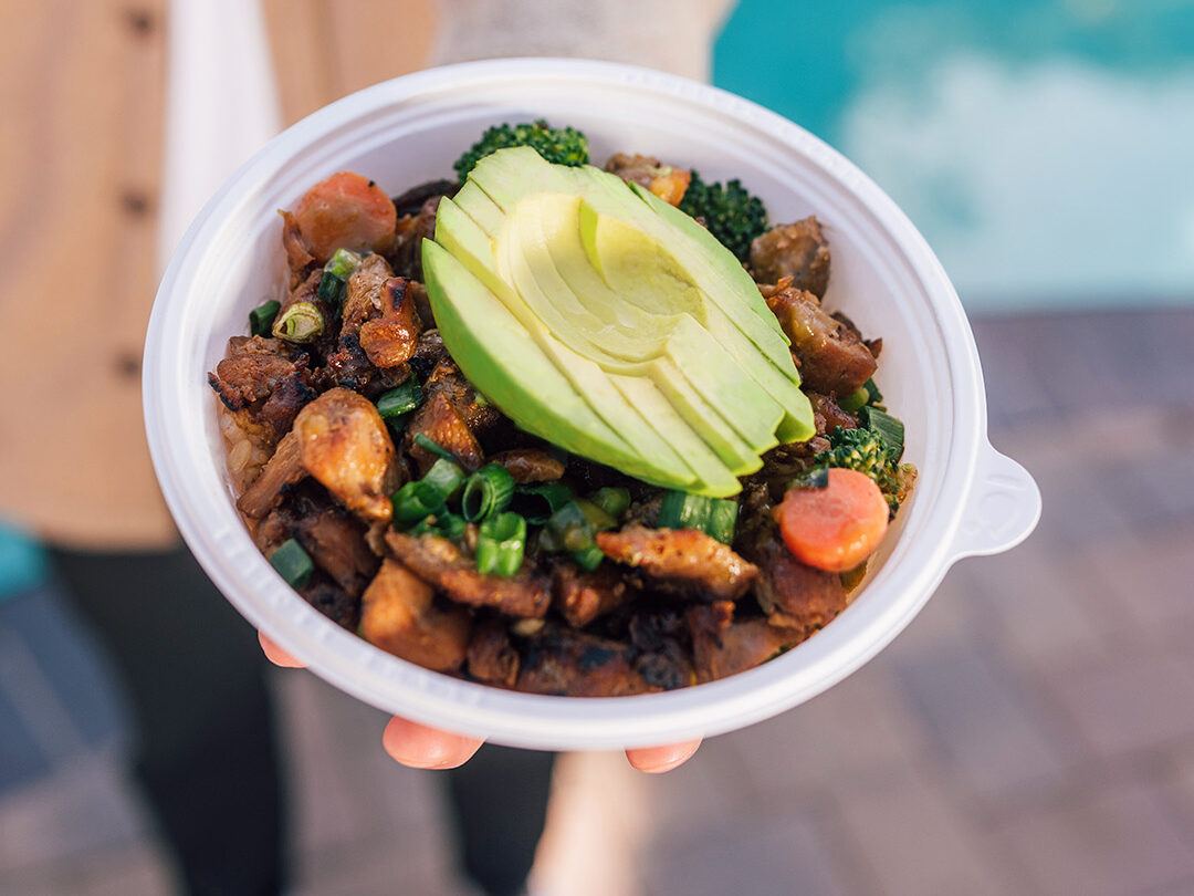 Person holding a bowl with rice, mix of meat, carrots and avocado - The Flame Broiler Menu
