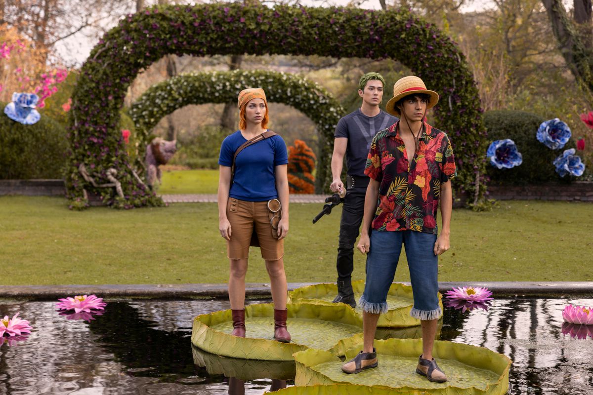 Nami (Emily Rudd), Zoro (Mackenyu), and Luffy (Iñaki Godoy) stand on lily pads in a colorful garden in Netflix’s One Piece