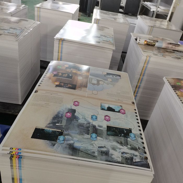 Stacks of poster-sized maps, game components destined for the Divinity Original Sin board game.