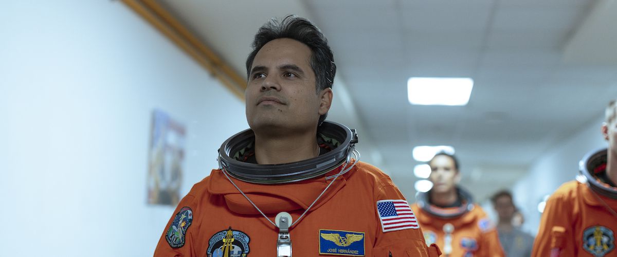 Michael Peña as José M. Hernández walking down a hallway in an orange spacesuit in A Million Miles Away.