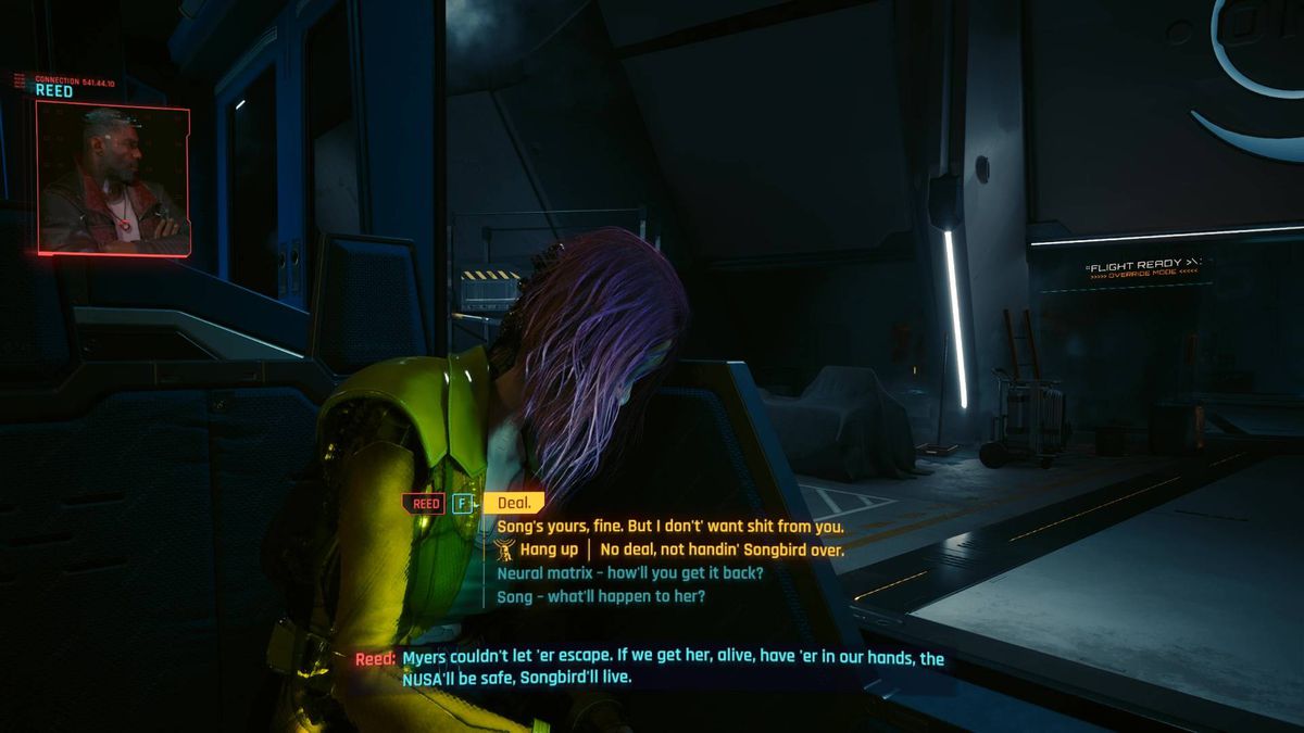 Songbird sits at a desk in a dark room during one of the Cyberpunk 2077 Phantom Liberty endings.
