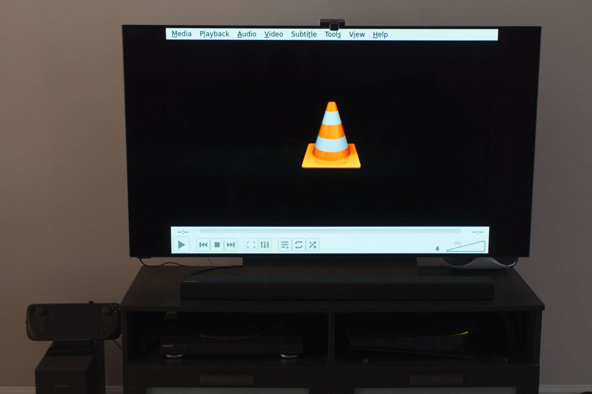 A photo of a 55-inch television with the VLC media player app shown on it. It is being powered by a Steam Deck with a USB DVD player plugged into its dock.