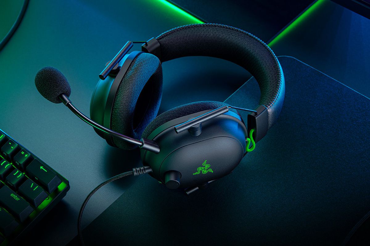 An image of the Razer BlackShark V2 wired gaming headset resting on a desk. The room is filled with the glow of a green light.