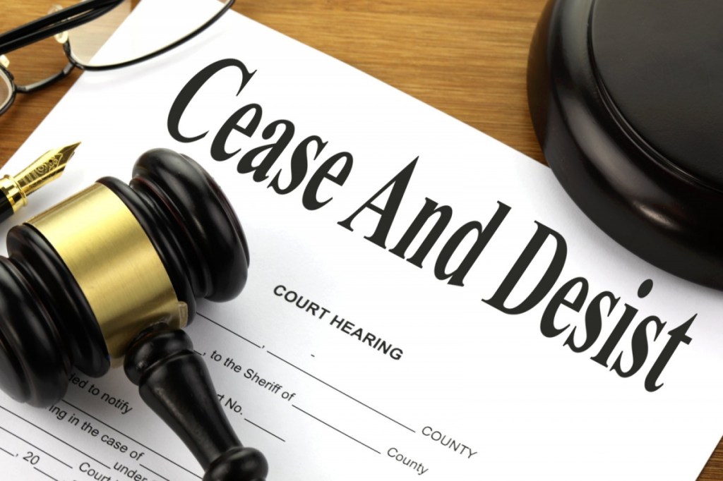 a court hearing form with cease and desist written at the top together with a gavel, block, pen and glasses.