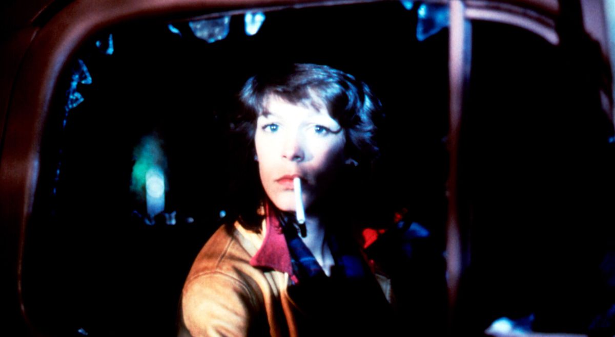 Jamie Lee Curtis, cigarett dinglande från hennes läppar, sitter lugnt i en bil med fönstret krossat i John Carpenters The Fog