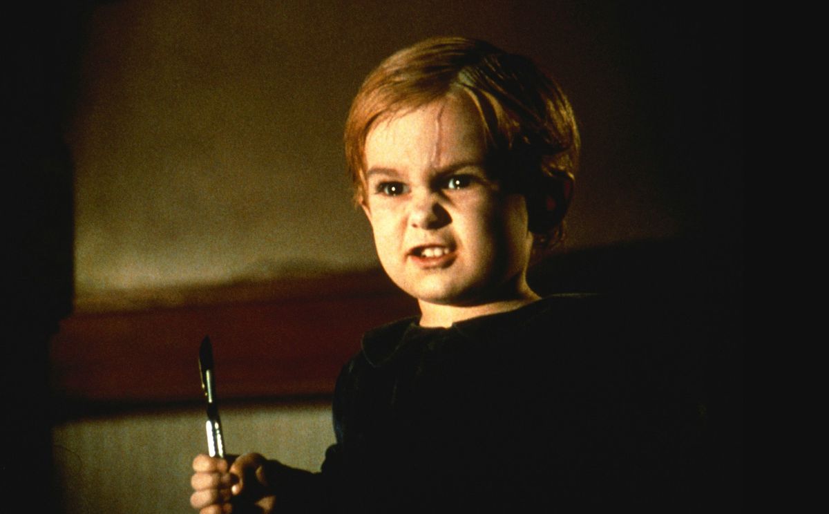 Malček s posmehljivim nasmehom na obrazu, rumeno brazgotino, ki teče po čelu, in skalpelom v glavi iz filma Pet Sematary iz leta 1989