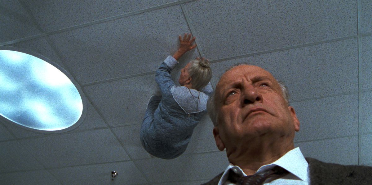 Джордж К. Скотт ходит по больнице, не обращая внимания на то, как седая женщина ползет по потолку над ним в «Экзорцисте III».