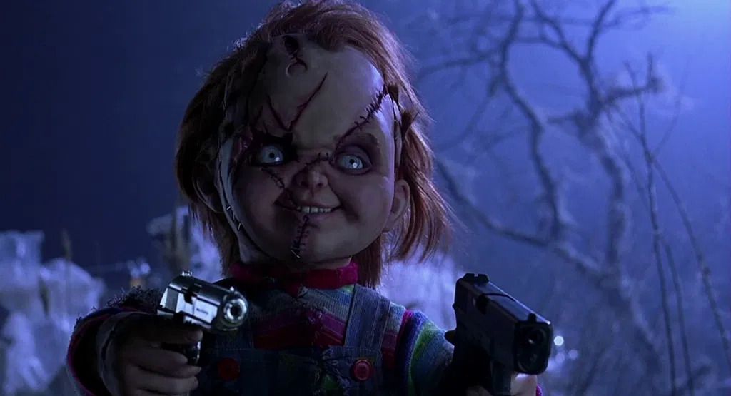 The Chucky doll dual wields pistols and looks past the camera in Bride of Chucky.