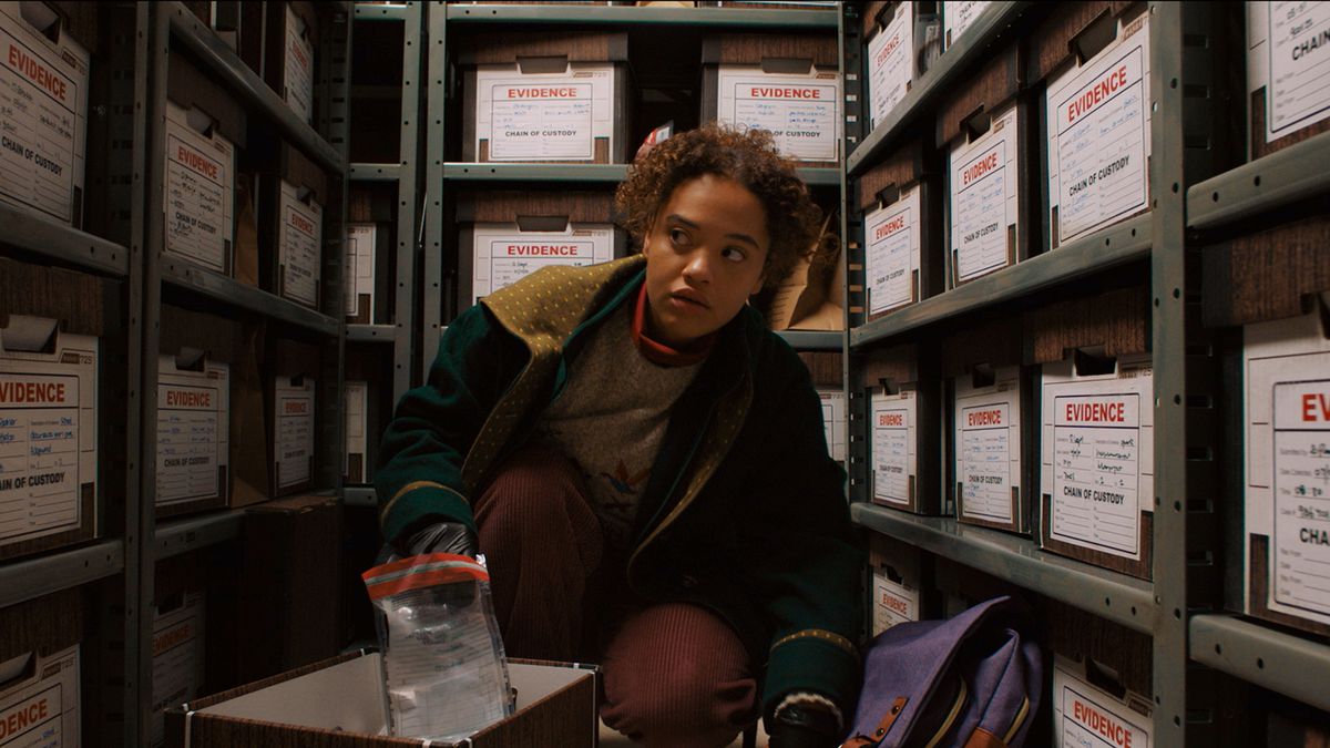 Kiersey Clemons as Susie kneeling in a closet filled with boxes labelled evidence in Susie Searches.