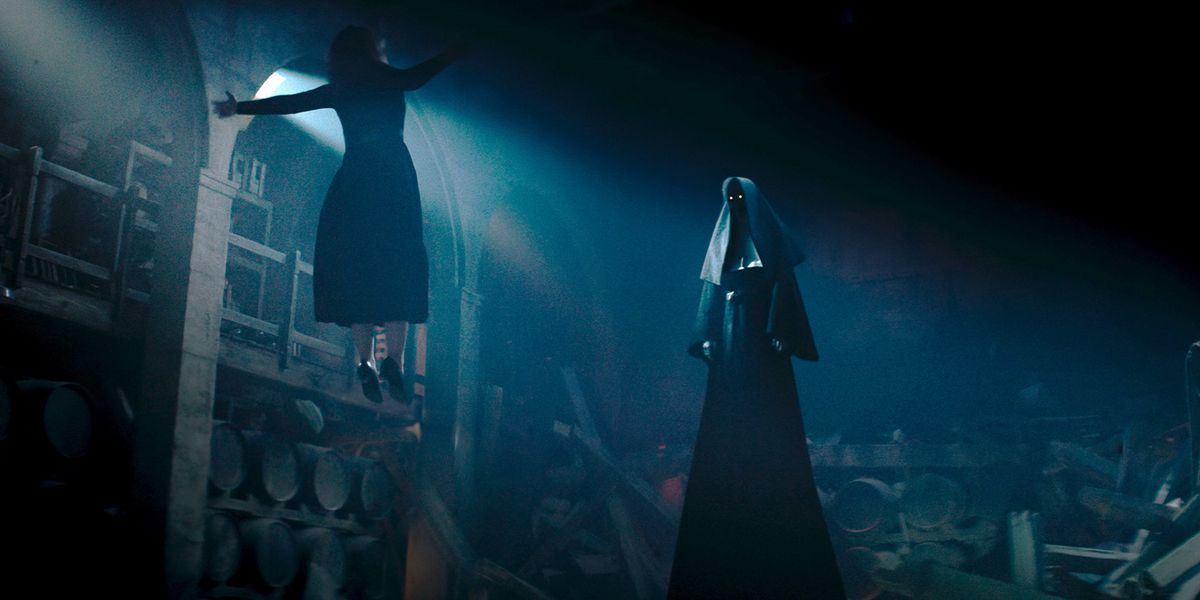 A woman floats helpless in front of a tall looming figure with glowing eyes in a nun outfit in The Nun 2.